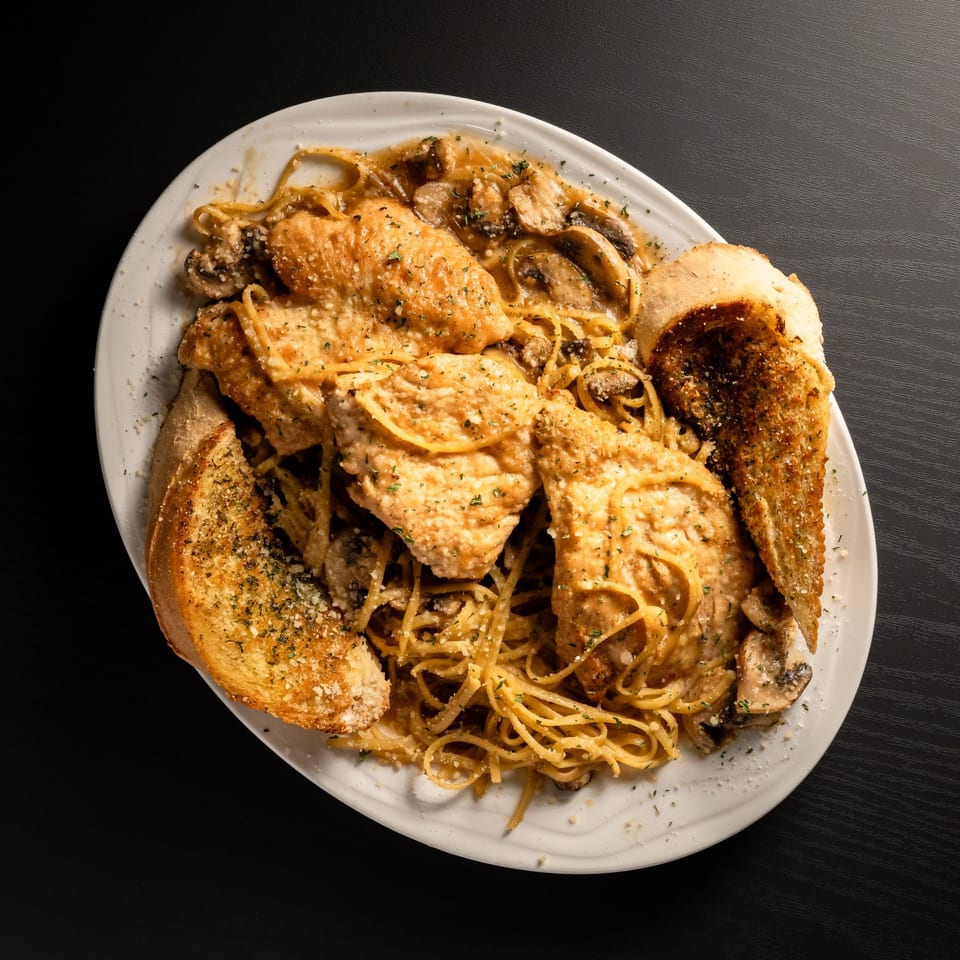 San Marino Italian Restaurant's chicken and mushroom pasta with garlic bread on a white plate.