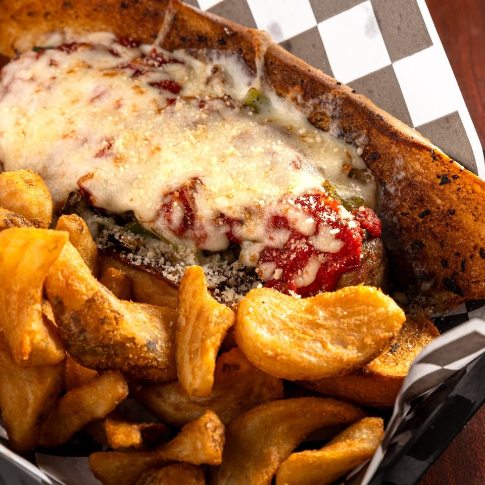 A San Marino Italian Restaurant meatball sub with melted cheese and sauce, served with golden potato wedges.