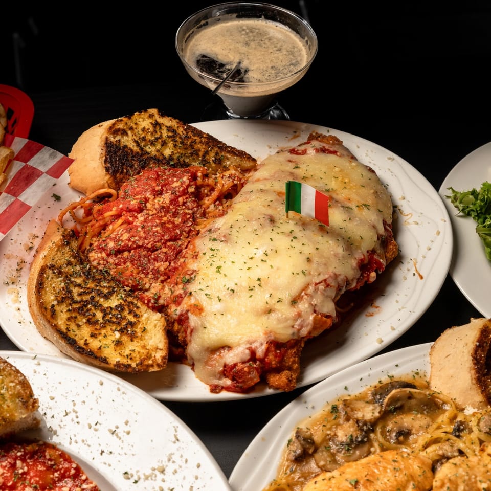 Chicken parmesan with spaghetti, garlic bread, and a cocktail on a dark background.