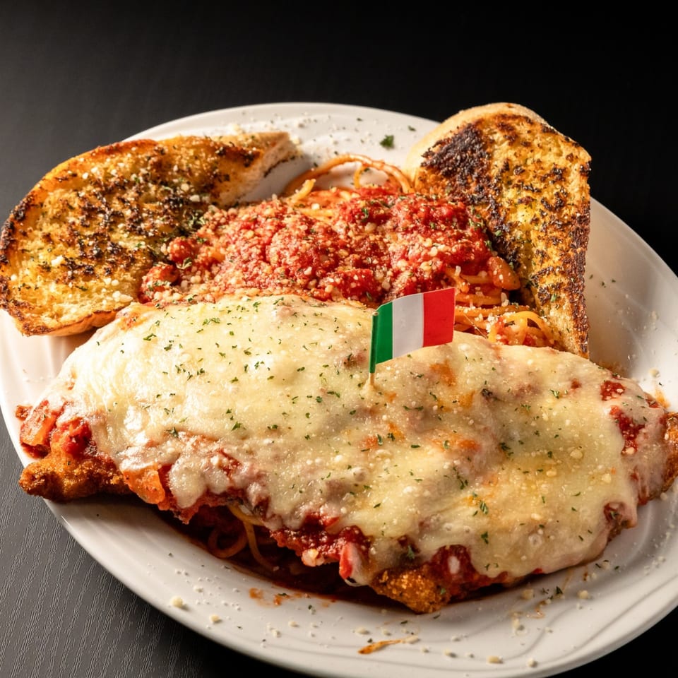 Chicken parmesan with spaghetti, marinara sauce, melted cheese, and garlic bread, garnished with an Italian flag.
